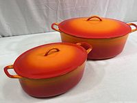 Two cast iron Dutch ovens with lids, one larger Descoware and one smaller FE Belgium, orange to red gradient enamel finish