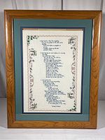 Overall view of the framed needlepoint featuring poem text and floral border inside wood frame with double matting.