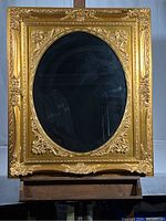 Full front view of the large oval mirror with an ornate gold rectangular frame, showing the beveled mirror surface and detailed carvings on the frame.