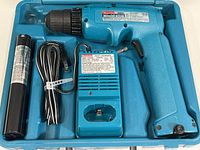 Makita cordless drill, battery, and fast charger all placed inside a blue molded plastic carrying case.
