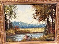 Front view of the framed oil painting showing the river, trees, and sky scene with signature in lower right.