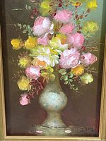 Close-up of the floral arrangement, showing pink and yellow roses in a ceramic vase with a dark background.