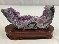 Front view of a curved purple amethyst geode with crystalline formations on wooden stand showing crystal details and colors.