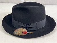 Front view of the black felt Stetson fedora hat showing the ribbon hatband, bow, and attached feather with Stetson pin