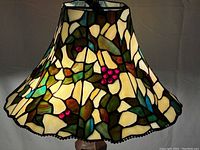 Close-up of stained glass shade showing green leaf and red berry vine pattern and metal ball fringe edge.