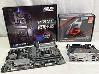 Two motherboards displayed in front of their original retail boxes, showing the ASUS Prime H570-Plus and ASRock X570 Phantom Gaming-ITX/TB3 boxes, the boards, and some cables.