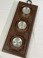 Full view of the rectangular faux wood panel with three circular brass-cased gauges arranged vertically, showing retro style and overall condition.