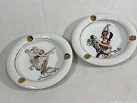 Two round white ceramic Trader Vic's tiki bar ashtrays side by side, showing their vintage dancing couple illustrations and gold accents.