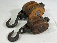 First image showing two wooden block and tackle pulleys with metal hooks and wooden bodies on a white background.