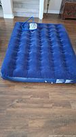 Blue double size air mattress with tufted flocked top and rubberized bottom, blue foot pump attached by hose on top of mattress