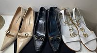 Three pairs of designer shoes displayed side-by-side: beige Manolo Blahnik heels, black Car Shoe loafers, and white Wishbone collection sandals.
