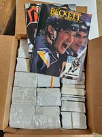 Box containing numerous bundles of hockey cards wrapped in plastic and rubber bands, stacked double layer.