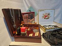Wide view of the wooden box with assorted men's items: chains, cufflinks, pocket cutters, pipe, aftershave bottle, button covers, keychains, and cigar box.