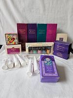 Lot contents showing boxes of Tribute, Intrigue, Genji, and Acapella foaming bath and shower gels, Mary Kay candle, aromatic oils set, body powder tubes, and Acapella perfume box.