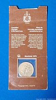 Full view of sealed coin in original cardboard holder showing front packaging with bilingual text and Olympic emblem