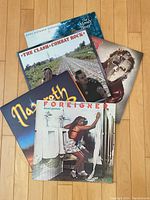 Six vinyl record album covers visible arranged on floor, featuring The Moody Blues, The Clash, Nazareth, Foreigner, Quiet Riot and one partially visible album.