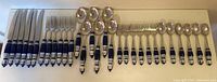 Full layout of the flatware set on a white surface showing knives, forks, and spoons with blue and white ceramic handles.