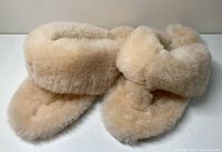 Top and side views of a pair of beige Australian sheepskin flip flop slippers with plush furry texture and padded straps.