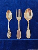 Set of two spoons and one fork arranged side by side on blue fabric background showing front view of silverware.