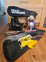 Full layout of sports equipment including roller blades, bags, racket, balls, mitt, boomerang, and badminton gear