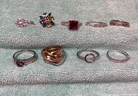 Photo showing all 9 rings arranged in two rows on a towel, showing various gemstones and band styles.