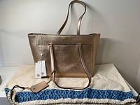 Tory Burch Robinson Metallic Small Tote in rose gold color with long shoulder straps, matching luggage tag, and blue patterned dust bag.