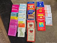 Photo showing 28 folded vintage European maps stacked in rows, with visible titles and colorful covers.