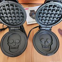 Two Dash Skull mini waffle makers open showing the skull-shaped cooking plates inside on a wooden surface.
