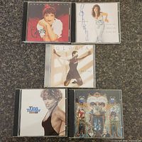Front view of five CD cases arranged on carpet, showing album artwork including Gloria Estefan, Tina Turner, and Michael Jackson.