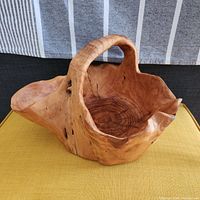 Front-side view of the large wooden root craft basket showing irregular edges, natural wood grain, and carved handle.