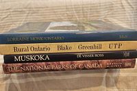 Stack of four coffee table books showing spines and titles: 'Ontario' by Lorraine Monk, 'Rural Ontario' by Blake Greenhill, 'Muskoka' by De Visser and Ross, and 'The National Parks of Canada' by Kraus and McNab.