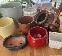 Top-front view of 7 colorful ceramic pots and a pottery strawberry pot on a wooden table