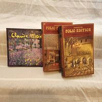 Three puzzles displayed side by side, two Waddington Folio Edition puzzle boxes showing historic interiors, and a Claude Monet jigsaw book with a floral Monet painting on the cover.