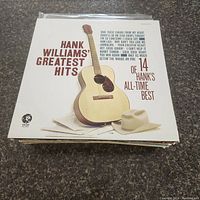 Photo of Hank Williams' Greatest Hits album cover featuring an acoustic guitar and cowboy hat on a white background.