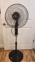 Full view of the black standing fan with heavy base and metal wire blade guard.