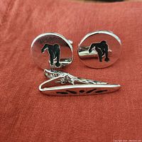 Pair of round cufflinks and tie clip laid out on reddish fabric background showing bowling theme design.