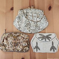 Top-down view of three vintage clutch purses: largest floral fabric clutch, medium gold sequin clutch, and small white beaded clutch with black design.