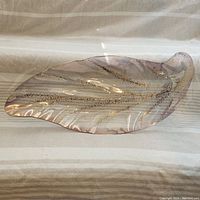 Top-down view of the elongated leaf-shaped glass platter showcasing the pink glass flecked with gold and blue glitter patterns.