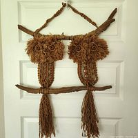 Front view of the vintage macrame wall hanging showing two owl figures with bead eyes on a white door background.