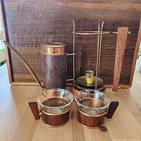 Full view of the tea set including kettle, candle warmer stand, and two glass cups resting on a wooden surface with wood back panel