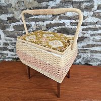 Front side view of the wicker sewing basket with embroidered lid and wooden legs.