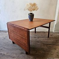 Table shown with one drop-leaf folded down and one leaf in tabletop position, vase on top for scale.