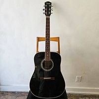 Full front view of black acoustic guitar on wooden chair