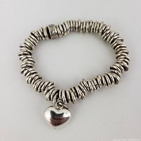 Full view of the sterling silver expandable bracelet laid in a circle showing disc-shaped beads and heart charm.