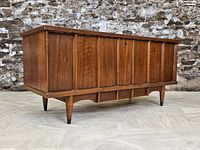 Front three-quarter view of walnut-finished chest showing vertical paneling and tapered legs.
