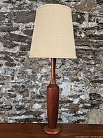 Full view of the teak table lamp with fabric shade against a stone wall background.