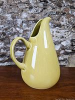 Front left-side angle view of the mustard yellow Russel Wright ceramic jug illustrating the spout, handle, and smooth glossy finish.