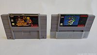 Front view of two SNES cartridges: Super Mario RPG: Legend of the Seven Stars (left) and Super Mario World (right) on white background