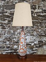 Full front view of the mid-century modern lamp showing the beige fabric shade, ceramic floral base, and teak wood base.