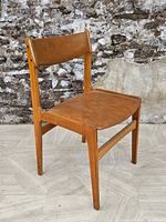 Front side view showing the teak wood frame and brown upholstered seat and backrest, against a stone wall and tiled floor.